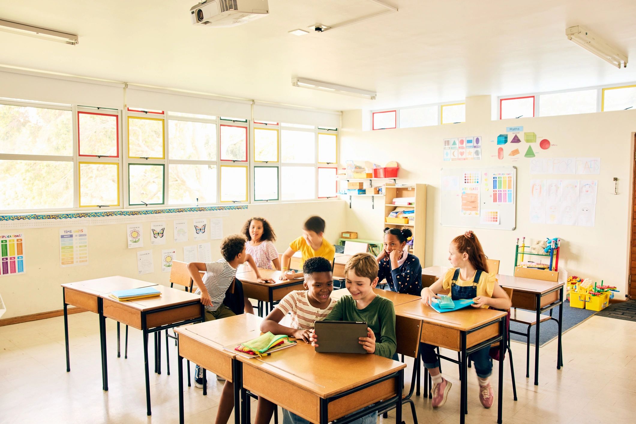 Children collaborating in a colorful classroom with a tablet and notebooks